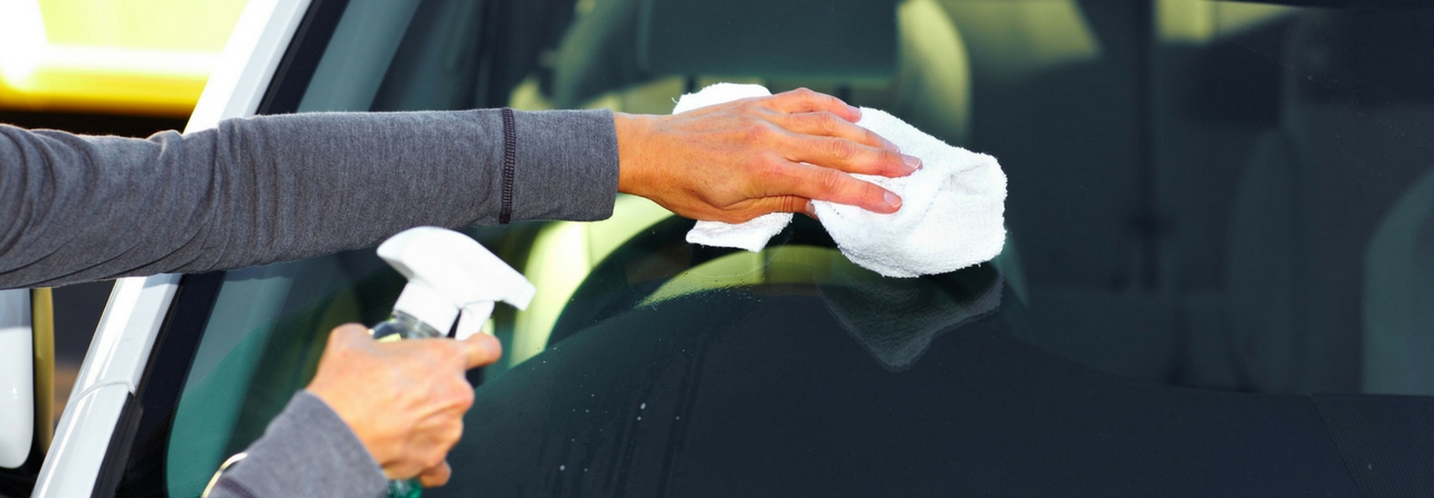 Man cleaning windshield with spray bottle and rag