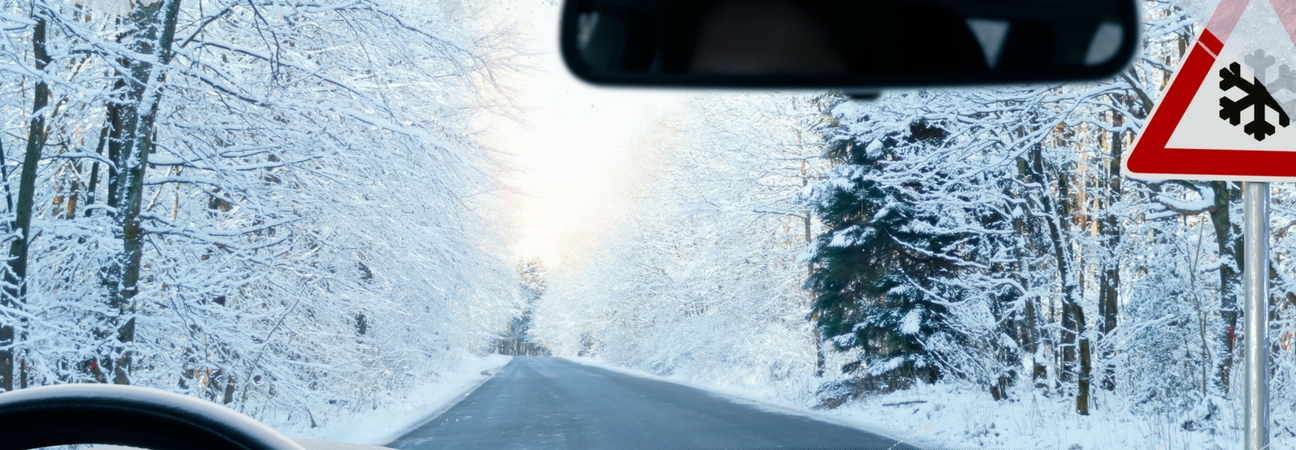 View of snowy roads and trees from behind the wheel of a car