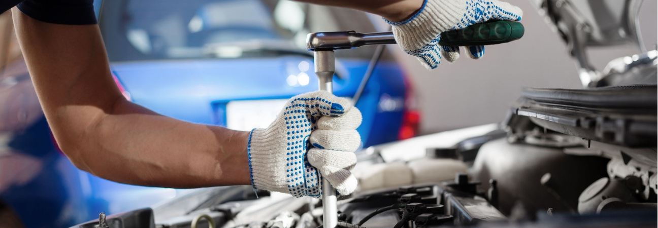 Man gripping underneath the hood of a car working on an engine.