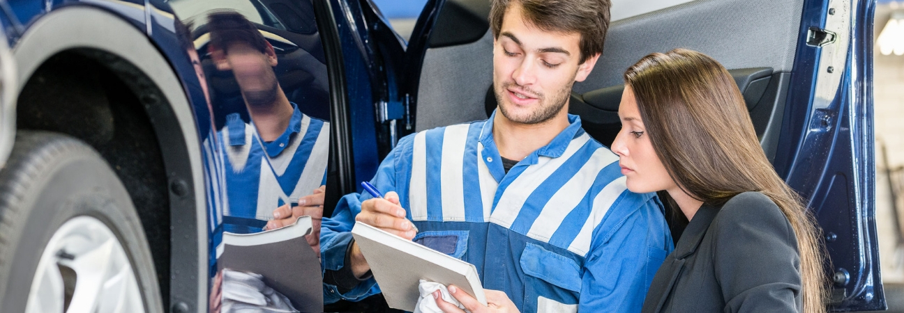 Man showing a woman a notepad next to her car in a body shop.
